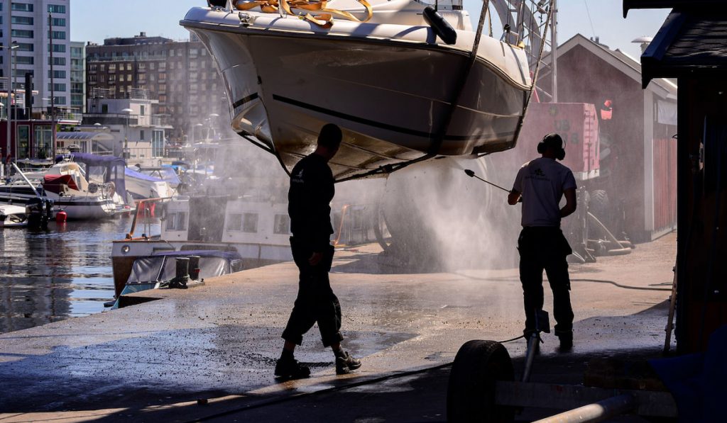 2 people pressure washing hanging boat in marina 