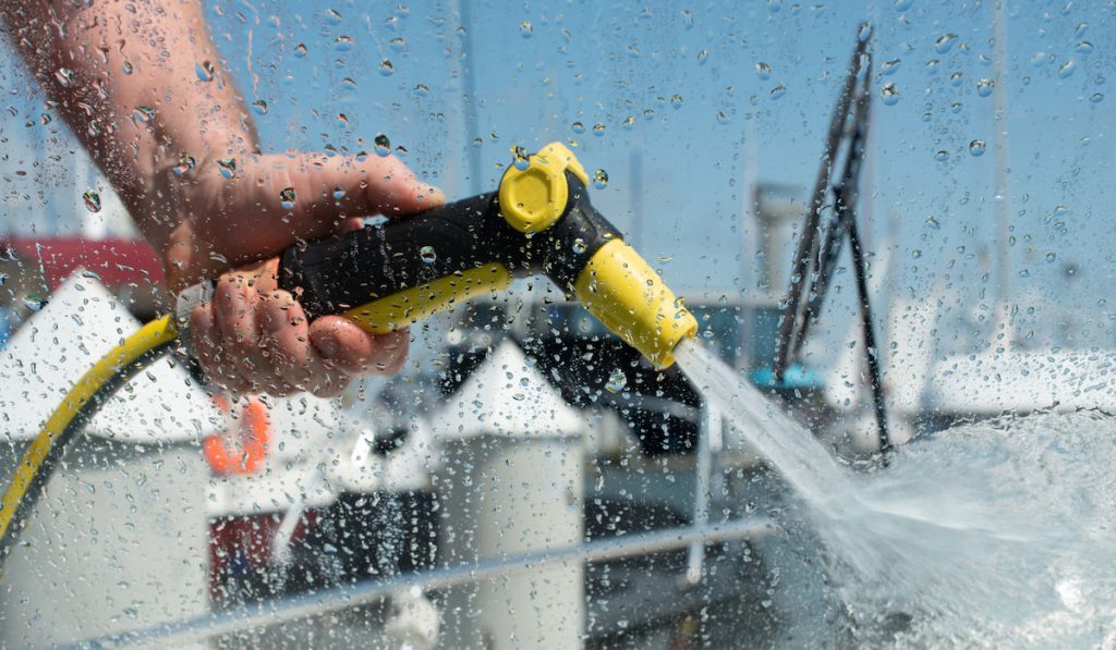 Hand holding water spray gun. Man washing boat with pressure water system.  