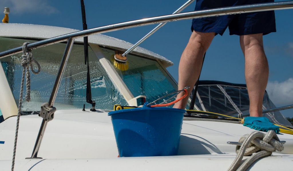 Man washing white boat with brush and pressure water system at pier. 