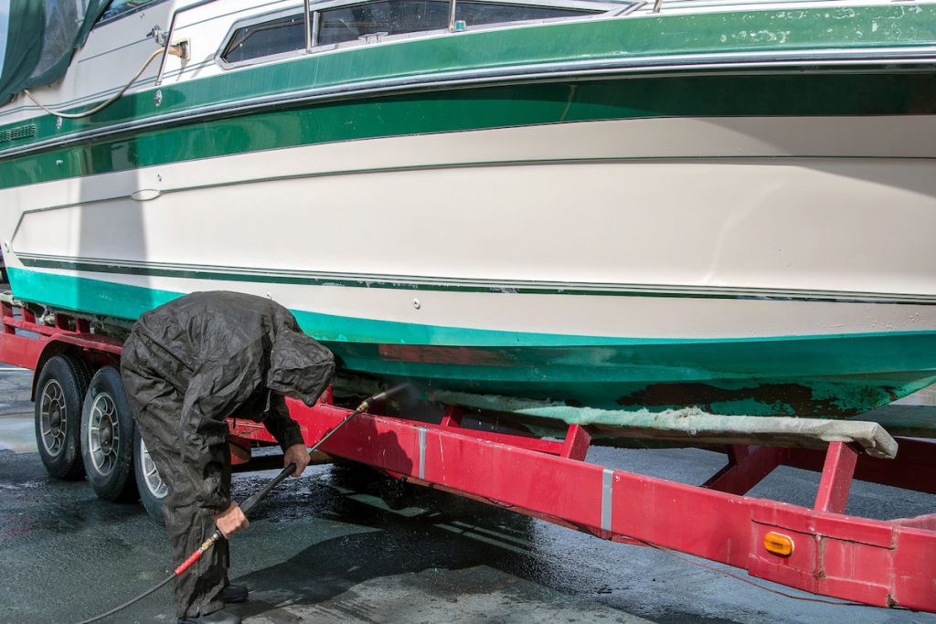 man wearing black waterproof rain suit while cleaning power boat hull with pressure washer 